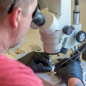 Conservator looking through a microscope to work on a strip of window lead