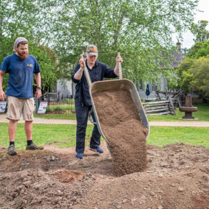 Erin Forys, Visitor Services Lead, dumps a pile of screened dirt as Archaeological Field Technician Josh Barber looks on.