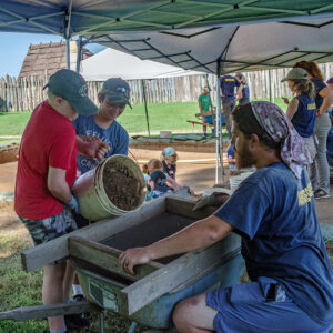 Two campers pour soil from the cellar excavations into a screen in order to look for artifacts.