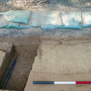 Rectangular trench cutting through an oblong feature within an excavation unit