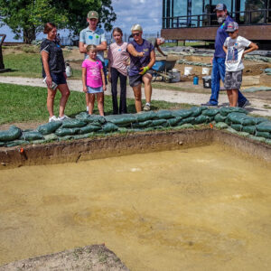 Staff Archaeologist Caitlin Delmas explains the upcoming burial excavation south of the Archaearium. The scored burial can be seen at the bottom of the photo.