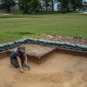 Archaeological Field Technician Ren Willis trowels away at the area around the burial south of the Archaearium.