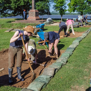 Field school students and staff excavate their squares in front of the Archaearium museum.