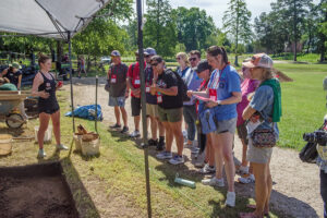 A field school student talks to visitors about the Archaearium site.