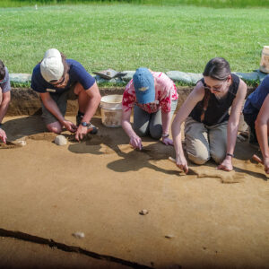 Archaeologists and Field School students digging at the north field excavation area. A glimpse of the 1906 water line trench is at bottom left.