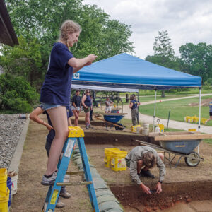 Field school student Lainey Harding uses a ladder to get a bit different perspective on an archaeological feature she's photographing.