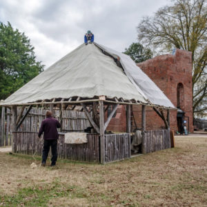 two men tying a canvas cover onto a wooden structure