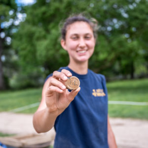 Archaeologist holds up glass wine bottle seal stamped with F*L