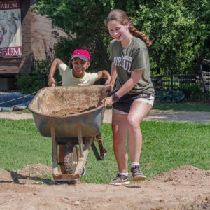 Field school student Grace Blondin-Kissel helps a camper push screened soil to the dirt pile.