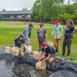 Field school students and archaeology staff form a bucket brigade to remove water from the barracks excavation site.
