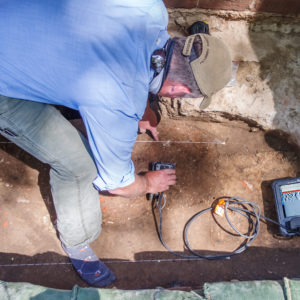 Archaeologist scanning a burial shaft with a handheld GPR unit