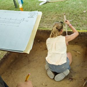 Field school student Natalie White measures the height of the various layers in a unit while another student records the measurements as a profile drawing.
