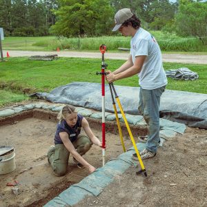 Archaeological Field Technician Katie Griffith and field school student Calvin Boulier set up surveying equipment at the barracks dig site.