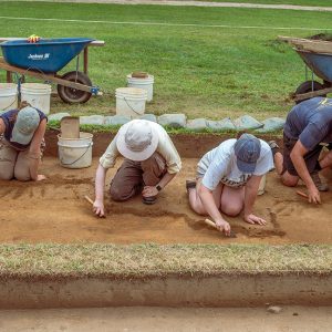 Field school students Julia Spencer and Jordan Searcey work with Staff Archaeologist Ren Willis and Archaeological Field Technician Josh Barber to carefully excavate a square just south of the Archaearium.
