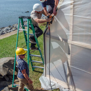 The archaeological staff staples the plastic covering to the burial structure frame.