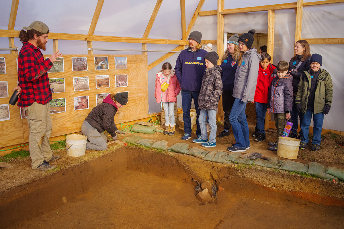 Archaeological Field Technician Josh Barber describes the excavations adjacent to the ticketing tent to some visitors.