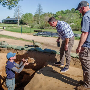 Staff Archaeologist Natalie Reid hands an iron object found in the 1608 ditch over to Director of Archaeology David Givens for examination. Senior Staff Archaeologist Sean Romo is at right.