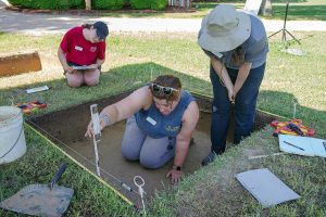 Archaeological Field Technician Hannah Barch instructs field school students Jennifer Wilkerson and Emily Yimer in the recording of layer dimensions at the dig in front of the Dale House.