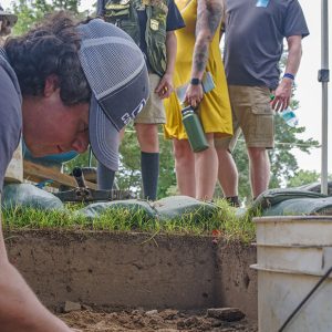 Visitors look on as field school student Calvin Boulier excavates an early 20th-century glass.
