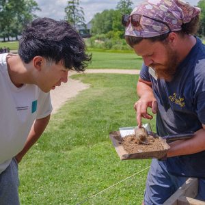 Archaeological Field Technician Josh Barber shares the discovery of an early 20th-century glass with a visitor.