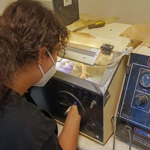 Field school student Emily Yimer tries her hand at air abrasion. Air abrasion is a technique that uses pressurized air to propel a fine stream of particles to physically remove corrosion from artifacts.