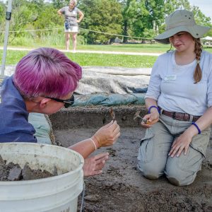 Staff Archaeologist Caitlin Delmas and field school student Amelia Fahl examine modern beer bottle glass found at the barracks site. The team affectionately named the type "Budware".