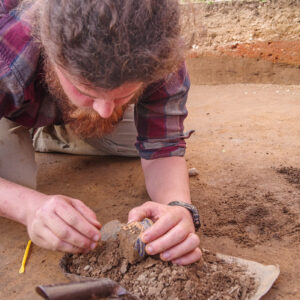 Archaeological Field Technician Josh Barber gently places the delft drug jar on a pan after excavation. The jar was found in the excavation tent adjacent to the ticketing tent.