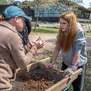 Staff Archaeologist Natalie Reid examines a partial pipe stem found by a Surry County High School student while screening southwest of the Archaearium.