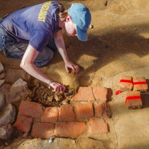 Staff Archaeologist Natalie Reid carefully excavates the chimney base of a ca. 1611 structure built on top of the 1607 burial ground. The chimney base needed to be removed in order to excavate a burial there.