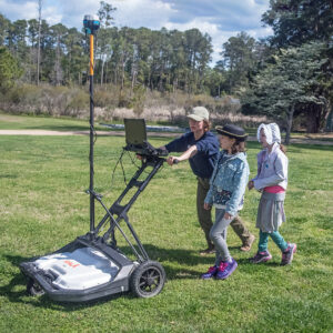 Archaeological Field Technician Ren Willis conducts a GPR survey of the grounds north of the Church Tower and explains the process to some visitors. Ren is using a GPR machine that contains two different frequency antennae brought by Dr. David Leslie of TerraSearch Geophysical.