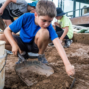 A camper scrapes away in the excavations south of the Archaearium.