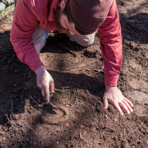 Archaeological Field Technician Josh Barber excavates a horseshoe found in one of the new excavation squares southwest of the Archaearium.