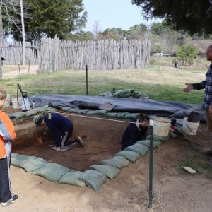 Senior Staff Archaeologist Sean Romo explains the dig north of the Church Tower to some visitors while Archaeological Field Technician Jack Schreiber and Site Supervisor Anna Shackelford conduct excavations.