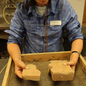 Senior Staff Archaeologist Mary Anna Hartley holds two paver bricks found during the north Church Tower excavations.