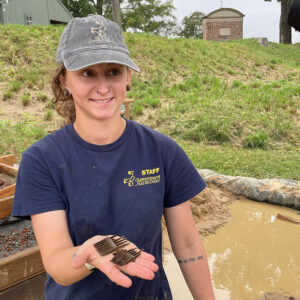 Archaeological Field Technician Ren Willis holds the wooden comb shortly after it was excavated.