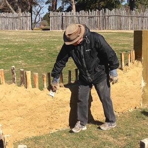 Archaeologist applying mud mixture to a low wall