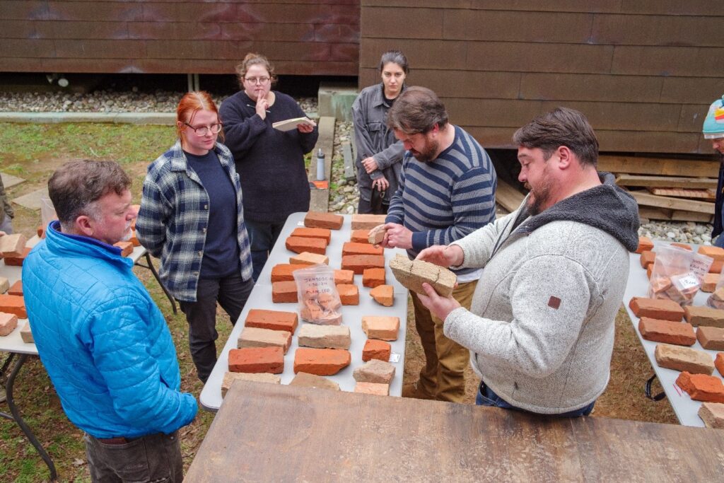 A group of people standing around a table with bricks on it. The people are examining the bricks