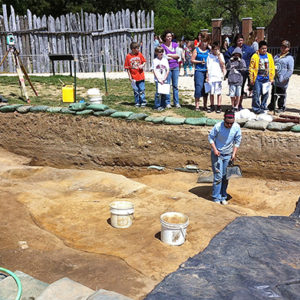 group of children and a guide watch an archaeologist excavating