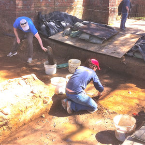 two archaeologists excavating with trowels and dustpans next to a brick church