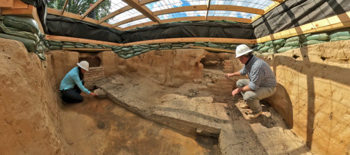 two archaeologists kneeling in a large unit covered with a wooden platform