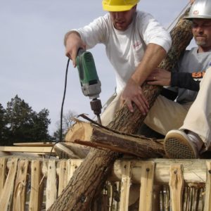 Man using a drill to secure building frame posts while another man holds them together