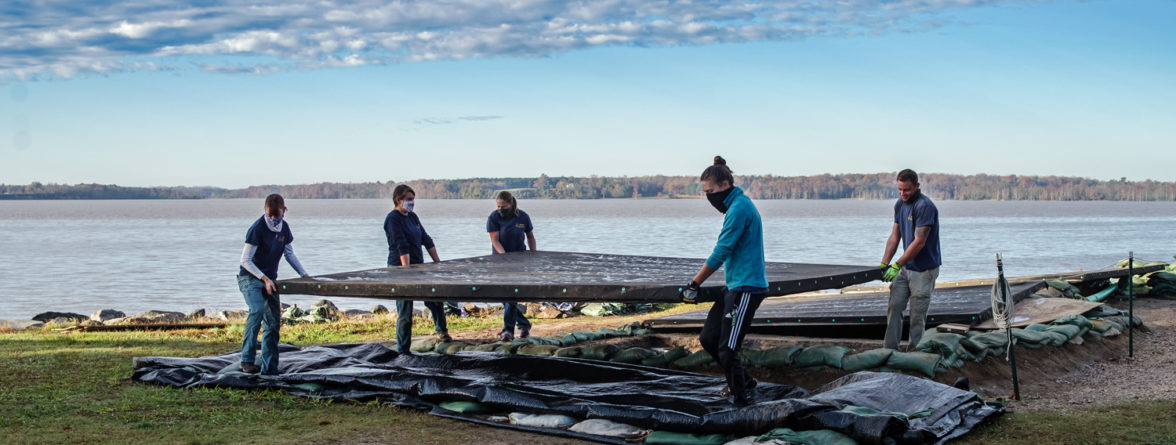 four archaeologists lifting a large cover over an excavation unit