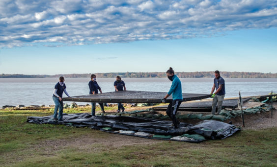 four archaeologists lifting a large cover over an excavation unit