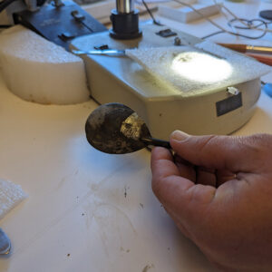 The spoon found in the Governor's Well. Senior Conservator Dan Gamble is removing corrosion to reveal the shine of the tin beneath it.