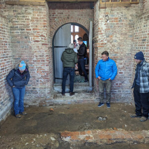 Senior Staff Archaeologist Mary Anna Hartley, Director of Archaeology David Givens, and Senior Staff Archaeologist Sean Romo discuss the upcoming excavations in the Church Tower. The eastern foundations of the 1617 church are visible running left/right in this photo and the large dark sections are likely the charred remains of the previous wood and plaster belfry destroyed during Bacon's Rebellion.