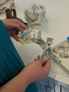 Curatorial Assistant Lauren Stephens holds the existing Portuguese faience dish (left half) with the newly mended pieces (right half). The two sections nearly mend together.