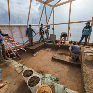 The archaeological team discusses the excavations east of the Memorial Church inside the former burial tent. The greenhouse effect of the tent allows the team to excavate on days when it would otherwise be too cold.