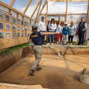 Archaeological Field Technician Ren Willis explains the context of the dig adjacent to the ticketing tent to some visitors.