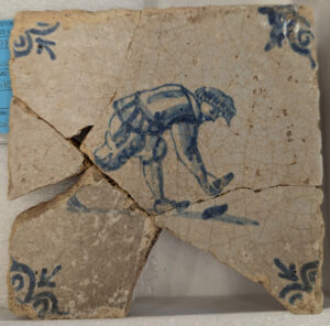 A recently mended Delft tile that might portray a man playing the game of quoits.