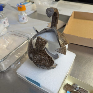 A partial Bartmann jug rests on a foam support created by Assistant Conservator Jo Hoppe as she mends it together.